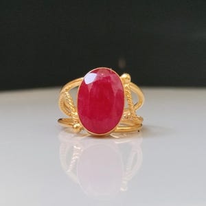 Peut inclure: Une bague en or ornée d'un grand rubis ovale. La monture de la bague présente un motif décoratif en forme de corde. Le rubis est d'un rouge vif, et la bague est posée sur un fond neutre.
