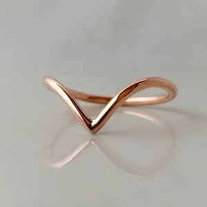 May include: A rose gold V-shaped ring. The ring has a smooth, polished finish and a delicate, minimalist design. The ring's shape is a gentle curve, creating a subtle and elegant look. The ring is likely made of a precious metal.