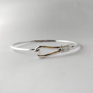 May include: A silver-tone bracelet with a hook clasp and gold-tone accents. The clasp is a hook and eye design. The bracelet has a simple, elegant design. The jewelry is suitable for everyday wear.