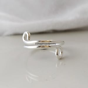 May include: A silver-colored ring with a unique, open design. The ring wraps around the finger with two curved ends. The text "Dishgemsandjewelry" is visible on the ring.