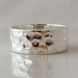 May include: A silver hammered ring with a 7mm width. The ring has a textured surface and a slightly rounded edge.