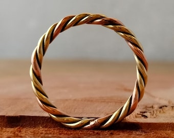 May include: A twisted ring made of three different metals: gold, copper, and silver. The ring is a simple design with a smooth finish.