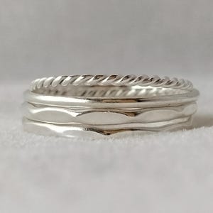 May include: Three silver rings stacked together. The top ring has a braided design, the middle ring has a wavy design, and the bottom ring is smooth.