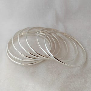 May include: A set of eight silver bangles stacked together. The bangles are smooth and shiny, and they are all the same size.