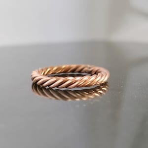 May include: A rose gold twisted band ring. The ring is made of a thick, braided wire.