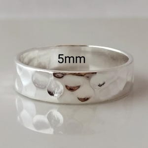 May include: A silver hammered band ring with a 5mm width. The ring is smooth and shiny.