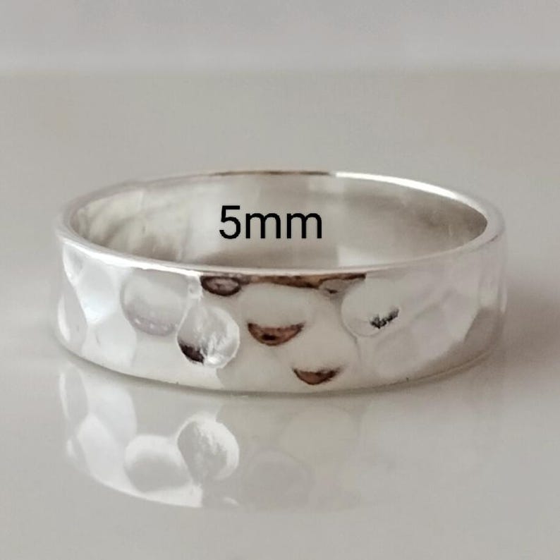 May include: A silver hammered band ring with a 5mm width. The ring is smooth and shiny.
