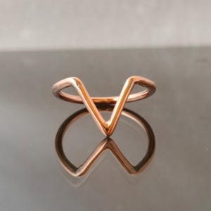 Puede incluir: Un anillo de oro rosa con un diseño en forma de V. El anillo es simple y elegante.