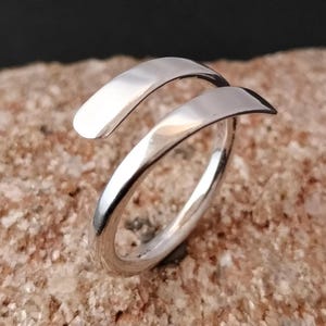 Könnte beinhalten: Ein silberner Ring mit einem einzigartigen Design, mit einem verdrehten Band, das sich um den Finger wickelt.