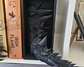 May include: Black dragon bookends with a detailed, textured design. The dragon's tail is curled around the bookends, and its head is facing forward. The bookends are sitting on a shelf with two books, one titled "Iron Flame" by Rebecca Yarros.