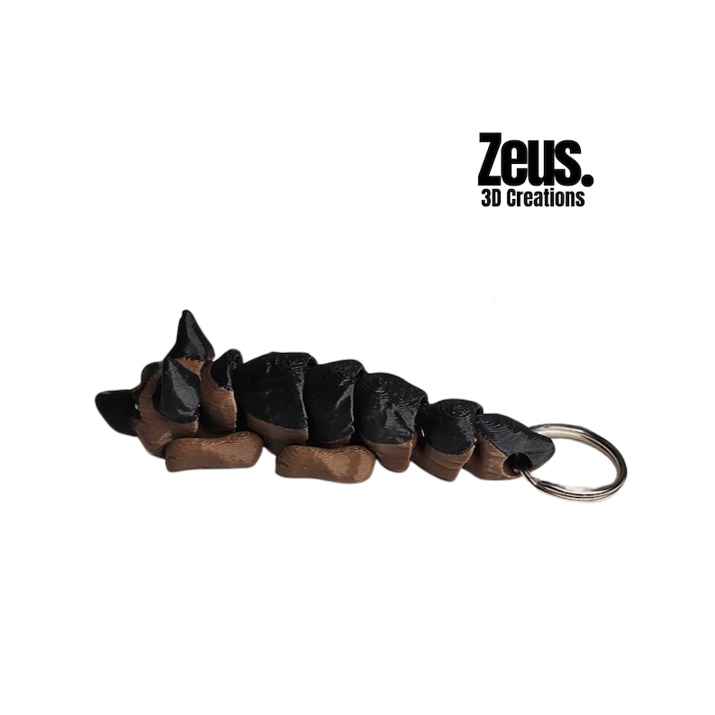 May include: A brown and black German Shepherd dog keychain with a silver key ring. The dog is curled up in a sleeping position. The keychain is made by Zeus 3D Creations.