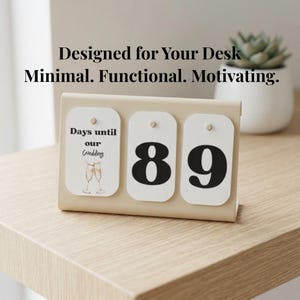 May include: A beige desk calendar with three white cards displaying the text "Days until our Wedding" and the numbers "89". The calendar is on a wooden surface. The text "Designed for Your Desk Minimal. Functional. Motivating." is at the top.