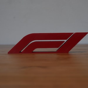 May include: A red plastic model of the Formula 1 logo. The logo is a stylised letter F with a curved line extending from the top.