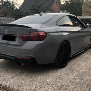 Può includere: Una BMW Serie 4 coupé grigia con cerchi neri e uno spoiler posteriore nero. L'auto ha un diffusore posteriore nero con due terminali di scarico.