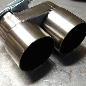 May include: A stainless steel dual exhaust tip with a clamp for attaching to a vehicle's exhaust system.