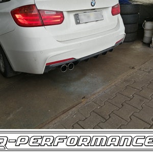 May include: A white BMW 3 Series with a black rear diffuser and dual exhaust tips. The car is parked on a gray brick surface. The image is labeled "D-PERFORMANCE".