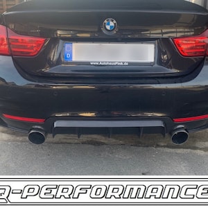 Może przedstawiać: Czarny BMW z dyfuzorem tylnym i podwójnymi końcówkami wydechu. Samochód ma niemieckie tablice rejestracyjne z napisem "D" i stronę internetową "www.AutohausFink.de". Samochód jest zaparkowany na szarej powierzchni asfaltowej. Obraz jest oznaczony "Q-PERFORMANCE®".