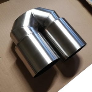 May include: A stainless steel dual exhaust tip with a U-shaped design. The exhaust tip has a polished finish and a round shape.