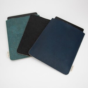 Peut inclure: Trois étuis pour tablette en liège. Les étuis sont en turquoise, noir et bleu marine. Chaque étui porte une étiquette blanche avec le texte "DOC ART FOR" imprimé dessus.