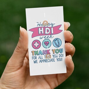 May include: A white card with the text "Happy HDI week" and "THANK YOU FOR ALL THAT YOU DO! WE APPRECIATE YOU!" in colorful lettering. The card features medical symbols: a cross, a heart, and a stethoscope.