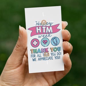 May include: A white card with the text "Happy HTM week" and "Thank you for all that you do! We appreciate you!" in various colors. The card also features medical symbols like a cross, heart, and stethoscope.