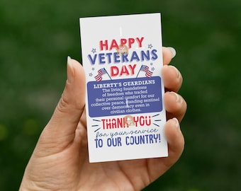 May include: A white card with the text "HAPPY VETERANS DAY" in red and blue, with American flags. The card also reads "LIBERTY'S GUARDIANS" and "THANK YOU for your service to our country!"