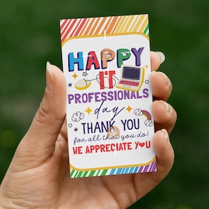 May include: A rectangular card with a colorful rainbow border is held in a hand. The card reads "HAPPY IT PROFESSIONALS day THANK YOU for all that you do! WE APPRECIATE YOU" with computer-themed graphics.