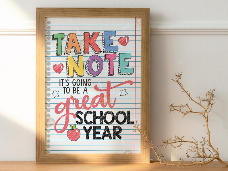 May include: A framed print with a white background and blue lines, resembling notebook paper. The text "Take Note It's going to be a great school year" is written in colourful letters with a red apple illustration.
