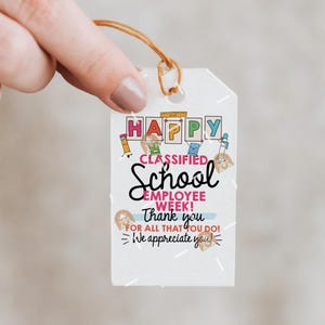 May include: A white gift tag with the words "HAPPY CLASSIFIED SCHOOL EMPLOYEE WEEK! Thank you for all that you do! We appreciate you!" in various fonts and colors. The tag is held by a hand.