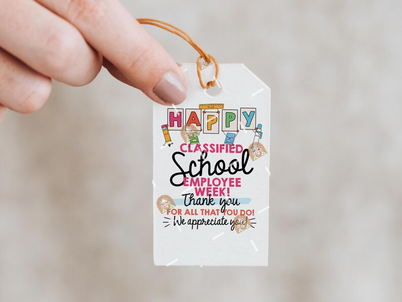 May include: A white gift tag with the words "HAPPY CLASSIFIED SCHOOL EMPLOYEE WEEK! Thank you for all that you do! We appreciate you!" in various fonts and colors. The tag is held by a hand.