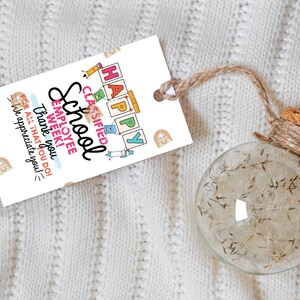 May include: A clear glass ornament filled with dried plant material, attached to a tag with the words "HAPPY SCHOOL EMPLOYEE WEEK!" The tag is white with colorful illustrations and a brown twine string.