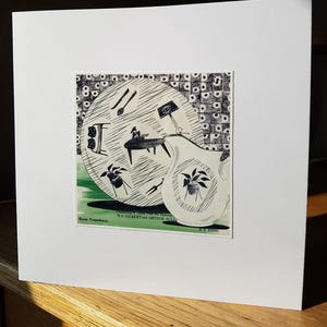 Può includere: Una stampa incorniciata con un'illustrazione musicale stravagante. L'opera d'arte include un trombone stilizzato, un tavolo con una figura e vari elementi musicali. Il testo "Bass Trombones" e "W.S. Gilbert and Arthur Sullivan" sono visibili.