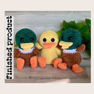 May include: Three crocheted duck plushies. One is yellow, and two are green with brown bodies. They have black eyes and orange beaks.