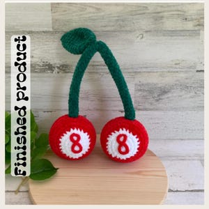 May include: A crochet plush toy shaped like two cherries with green stems and leaves. Each red cherry features a white circular center with a red number 8, resembling billiard balls. The text Finished product is printed vertically on the left.