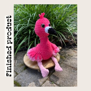 May include: A handmade, pink crochet flamingo with a black and white beak, sitting on a wooden base. The flamingo has large, round eyes and pink and light pink accents. The text "Finished product" is visible on the left side of the image.