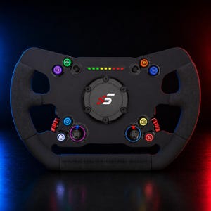 Puede incluir: Un volante de carreras negro con un centro circular que muestra un logotipo con el número 5 en blanco y rojo. El dispositivo incluye varios botones retroiluminados de colores, diales giratorios y una barra indicadora LED de revoluciones.