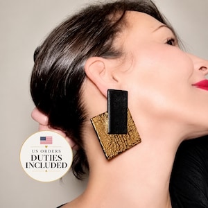 May include: A geometric earring featuring a rectangular black piece layered over a larger square piece with a textured gold finish. The gold surface displays a distinct crackled pattern, creating a high-contrast look between the matte black and metallic gold elements.