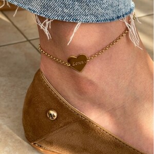 May include: Gold ankle bracelet with a heart-shaped charm engraved with the name "Loren".