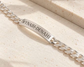 May include: A silver-toned curb chain bracelet featuring a central, slightly curved rectangular identification plate. The plate is engraved with the text WYNAIH-DENAHI in a clean, dark, sans-serif font, centered on the polished metal surface.