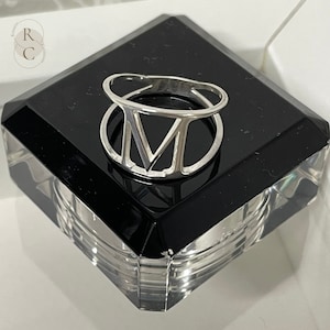 Może przedstawiać: Srebrny pierścionek z wzorem rzymskiej cyfry V. Pierścionek znajduje się na czarnym i przezroczystym stojaku.