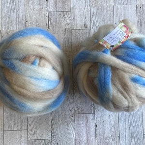 May include: Two balls of yarn in shades of blue, white, and brown. The yarn is arranged in a swirling pattern. One ball has a tag attached that reads "100% wool, 100g, 3.5 oz, 120m, 131 yds, hand dyed, superwash".