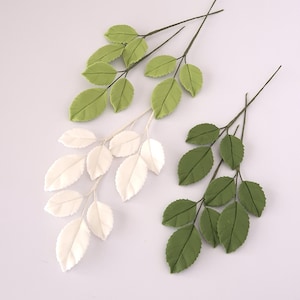 May include: Three artificial leaf sprigs are displayed. One has white leaves, the others have green leaves. The leaves have a textured finish and are attached to thin, dark stems. Ideal for craft projects.
