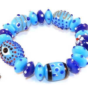 May include: A handcrafted bracelet made of blue glass beads. The bracelet features light blue, dark blue, and patterned beads with white and red details. The beads are strung together to create a circular design.