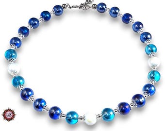 Puede incluir: Un collar de cuentas con una disposición circular de cuentas esféricas que alternan entre azul oscuro, azul claro y blanco. Cada cuenta está separada por pequeños espaciadores de metal plateado. El collar incluye un cierre de metal plateado.