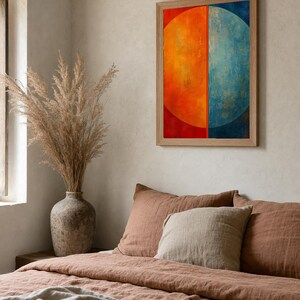 Könnte beinhalten: Ein rechteckiges Wandbild in einem hellen Holzrahmen mit einem geteilten kreisförmigen Design, das eine leuchtend orangefarbene linke Hälfte und eine texturierte blaue rechte Hälfte zeigt, platziert über einem Bett mit rostfarbener Bettwäsche.