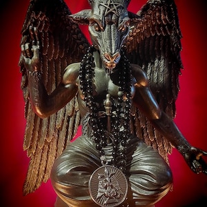 Könnte beinhalten: Eine bronzefarbene Statue von Baphomet, einer ziegenköpfigen Gottheit, mit großen gefiederten Flügeln, einem Pentagramm auf der Stirn und einer Perlenkette. Die Statue sitzt mit erhobener Hand und einem Anhänger mit detailliertem Emblem.