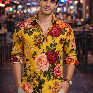 May include: Yellow button-down shirt with a vibrant floral pattern of red, pink, and orange roses and green leaves. The shirt has long sleeves and is paired with beige pants. A gold necklace and a brown watch complete the look.