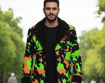 Puede incluir: Un abrigo largo con un llamativo estampado de camuflaje en verde neón, naranja y negro. El abrigo tiene cuello y puños negros. La persona lleva una camiseta negra, vaqueros negros y botas negras. La persona camina por un camino pavimentado.