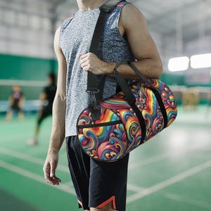 May include: A vibrant duffel bag featuring an abstract pattern in a rainbow of colours. The bag has a black shoulder strap and handles. The cylindrical bag is made from a durable material. The bag is being carried by a person.