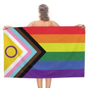May include: A rectangular flag displaying the Progress Pride flag design. The flag features a rainbow of colours, with a yellow triangle and a purple circle on the left. It also incorporates the colours of the transgender flag and those representing marginalised communities of colour.